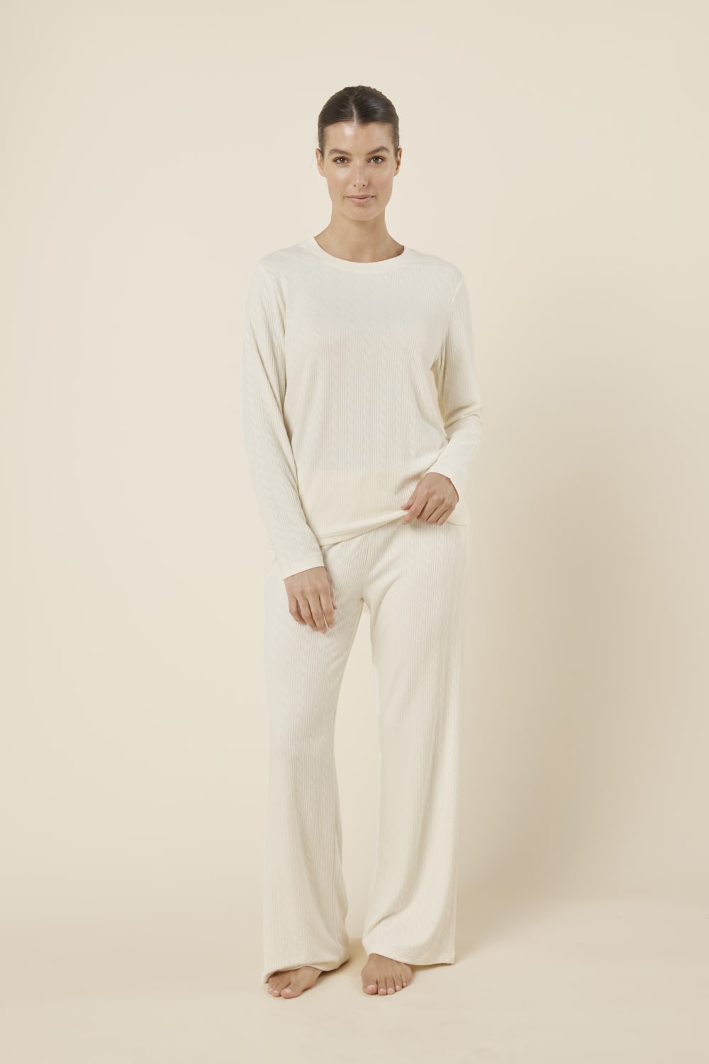 Woman wearing a ellie lightweight velour cable knit set ivory long-sleeve top and pants on a beige background front on view