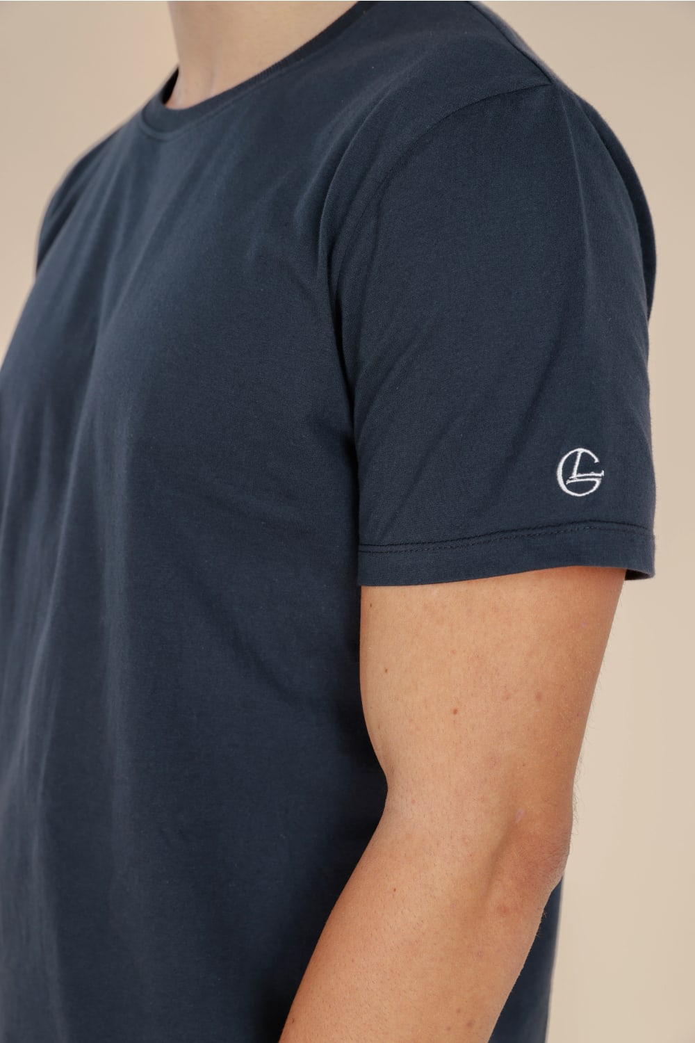 Navy blue t-shirt with a logo on the sleeve against a beige background