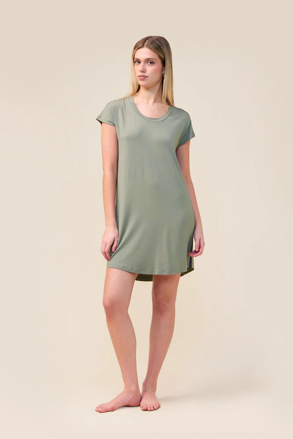 A woman modeling a short-sleeve, scoop-neck nightgown in sage green against a solid, warm beige studio background.