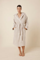 Woman wearing a striped adriana terry towel robe in biscuit colour standing against a plain background