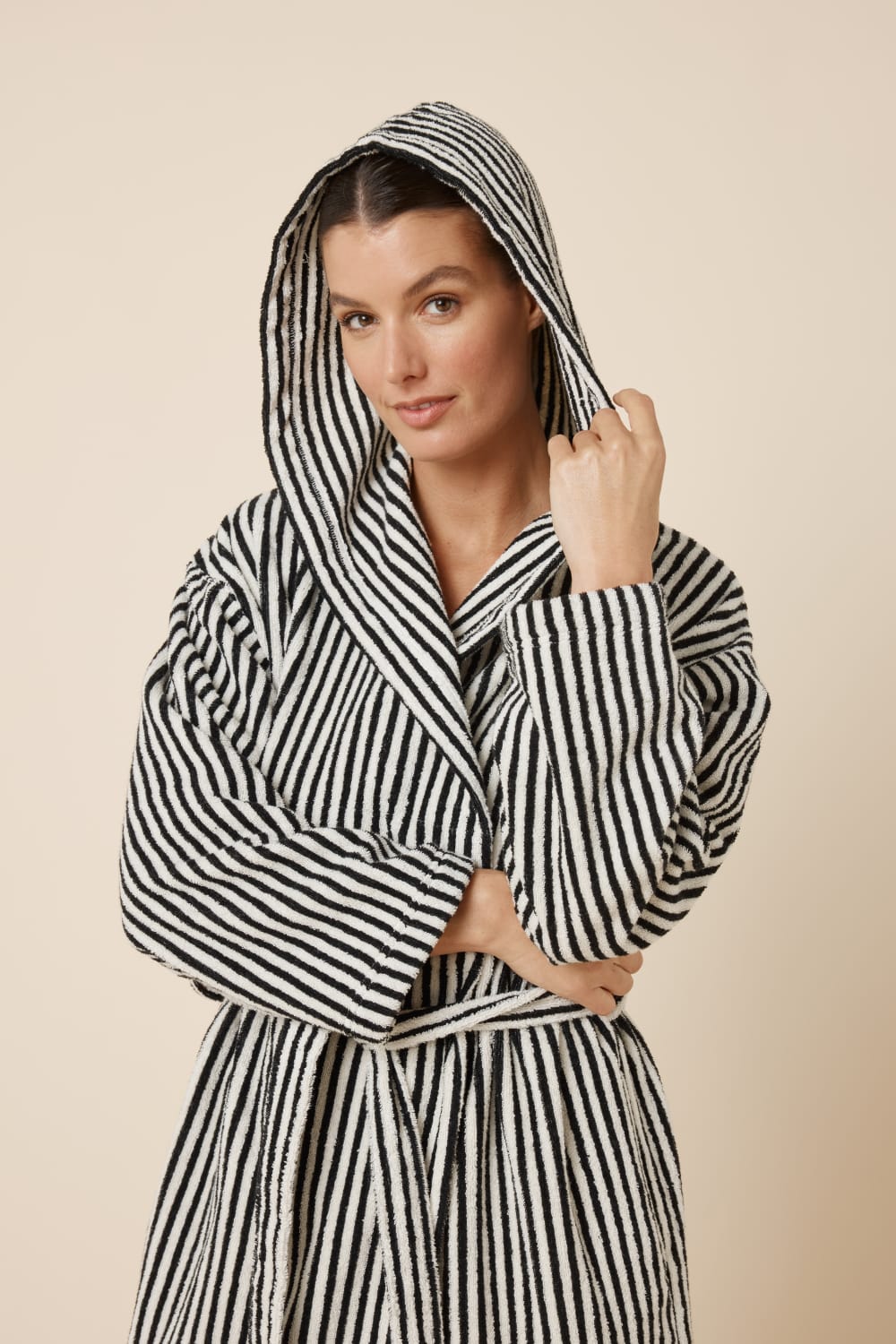 Woman wearing a striped adriana terry towel robe in black colour upper body view with her hold the hood which is on her head