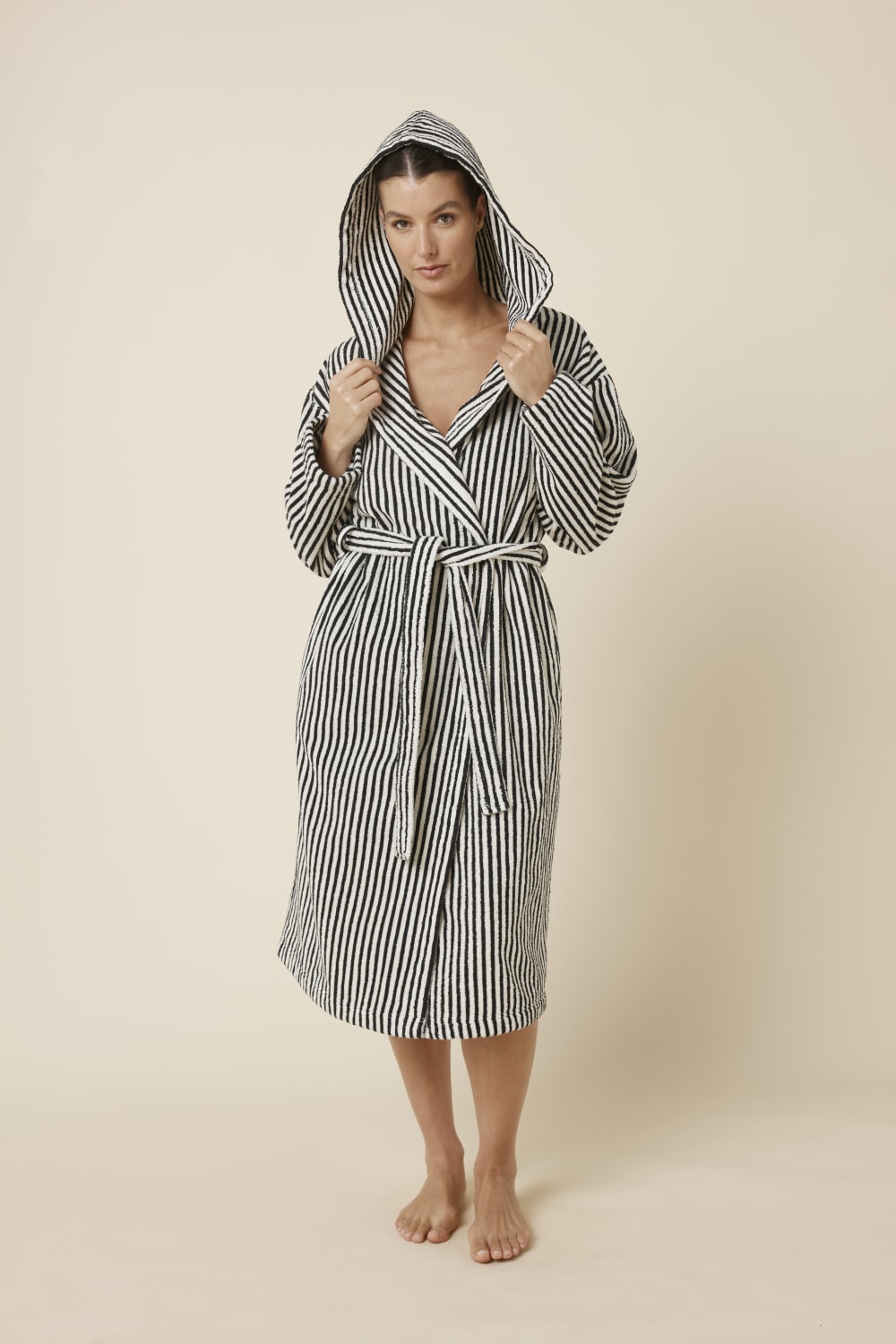Woman wearing a striped adriana terry towel robe in black colour front on view with hood on