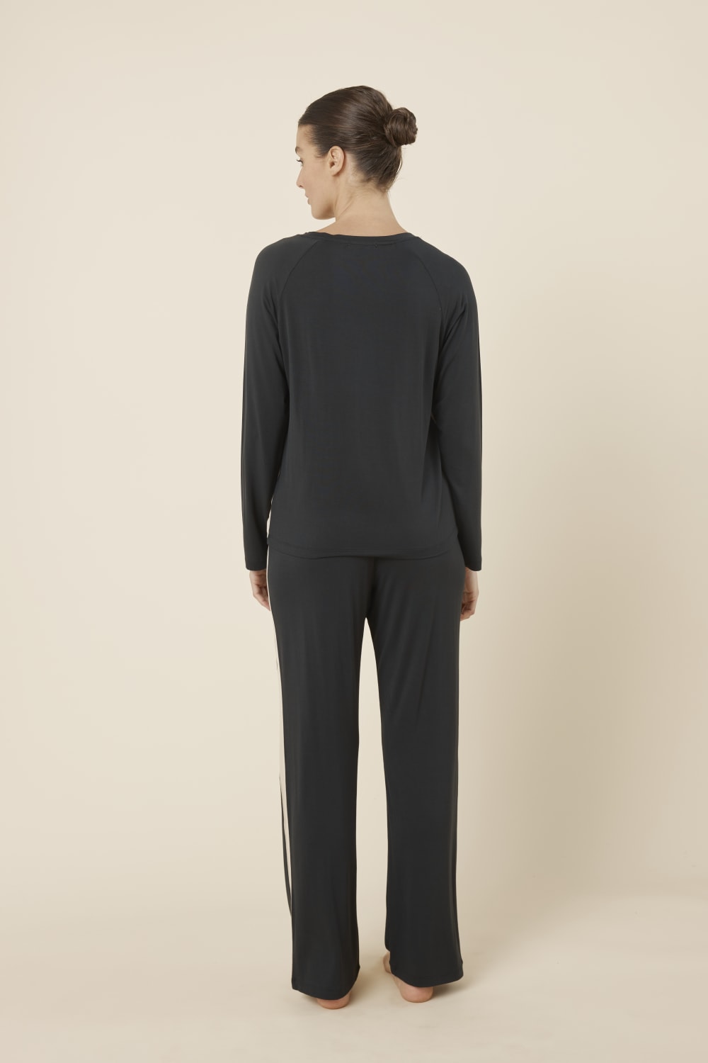 Woman wearing Anya Bamboo Sporty PJ Set Black standing with her back turned, showing the relaxed fit bamboo top and straight leg lounge pants.