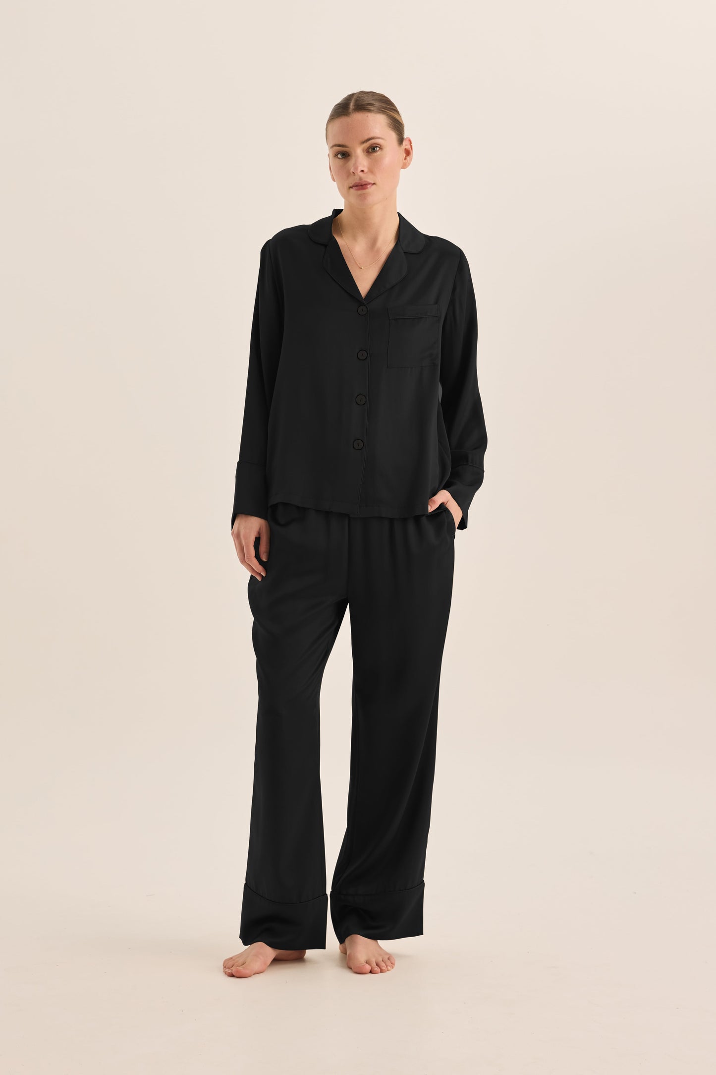 Woman wearing black Gingerlilly Sleepwear long sleeve pajama set, barefoot, on neutral background