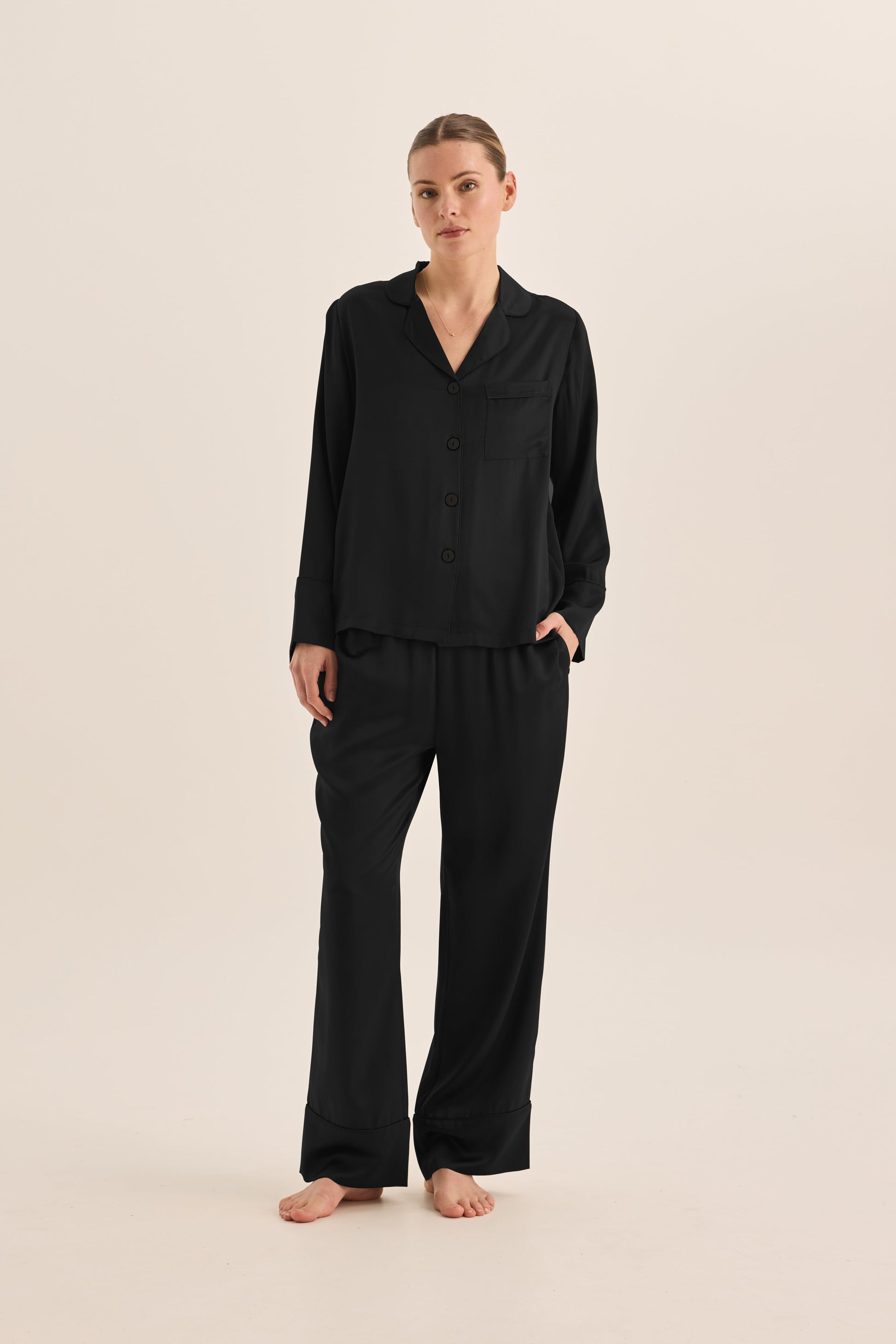 Woman wearing black Gingerlilly Sleepwear long sleeve pajama set, barefoot, on neutral background