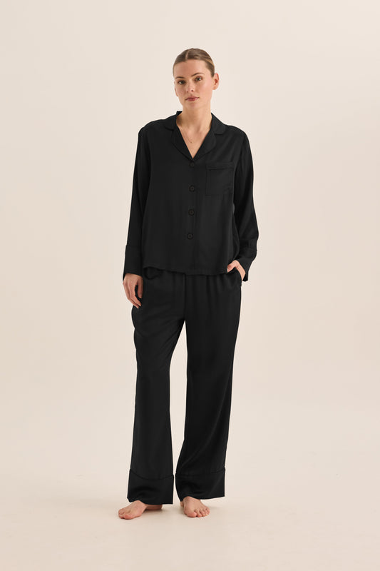 Woman wearing black Gingerlilly Sleepwear long sleeve pajama set, barefoot, on neutral background