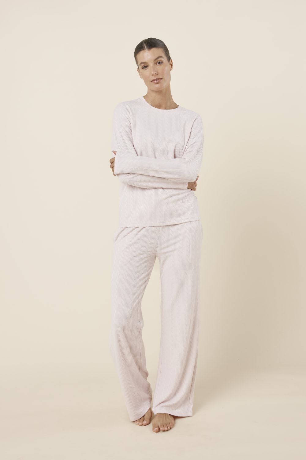 Woman wearing a ellie lightweight velour cable knit set pink long-sleeve top and pants on a beige background front on view with hands crossed