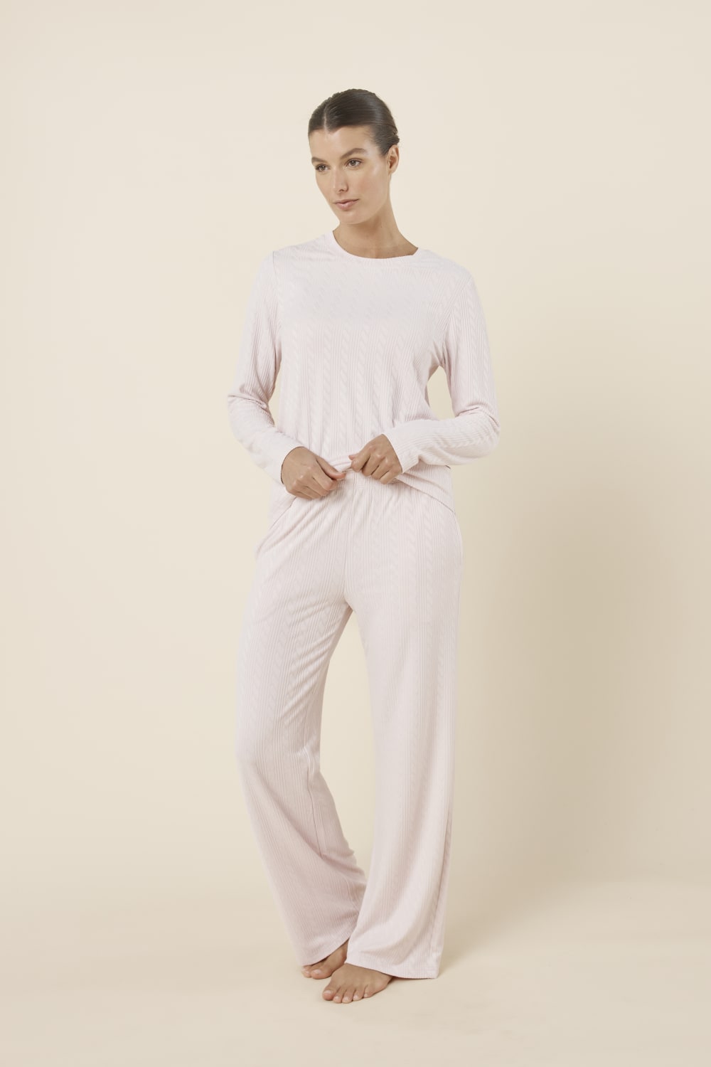 Woman wearing a ellie lightweight velour cable knit set pink long-sleeve top and pants on a beige background side on view