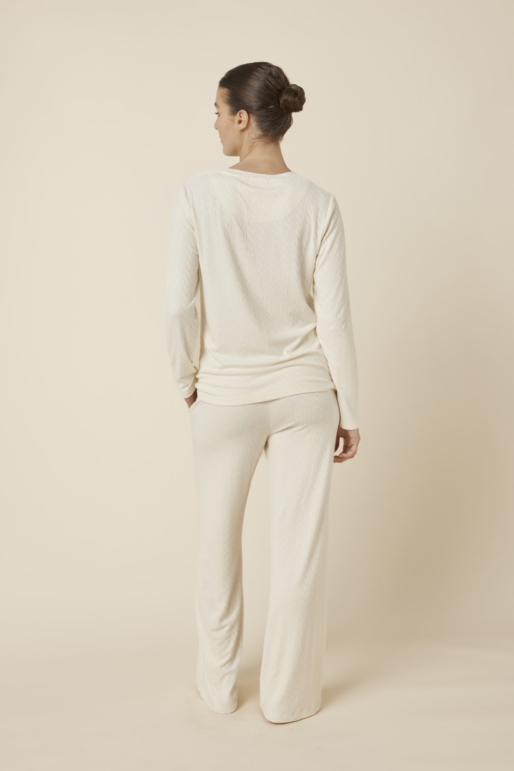 Woman wearing a ellie lightweight velour cable knit set ivory long-sleeve top and pants on a beige background back view