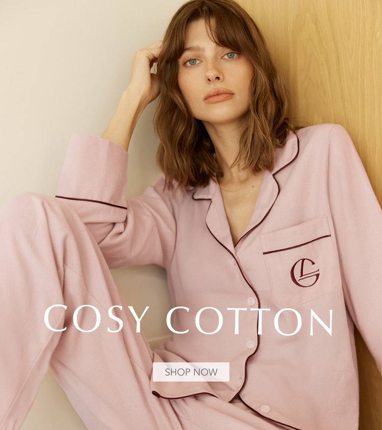 Woman wearing pink pajamas with a visible brand logo, sitting against a light-colored wall.