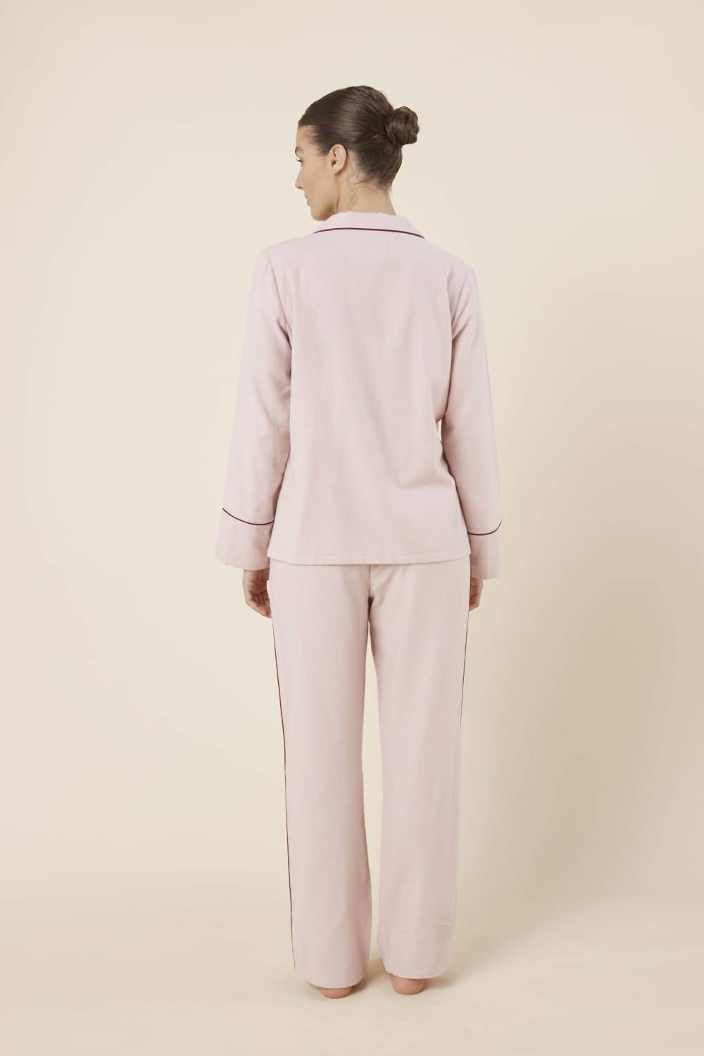 Woman wearing light pink isabella brushed cotton pyjama PJ set with a small red logo on a beige background back view