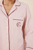 Woman wearing light pink isabella brushed cotton pyjama PJ set top with a small red gingerlilly embroidery logo on pocket with red piping detail and a beige background. 