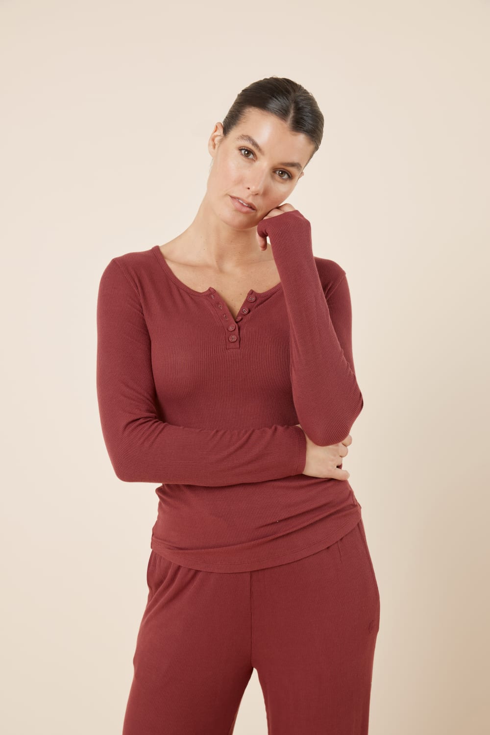 Woman wearing Lille Ribbed Long Sleeve Henley Top Burgundy leaning slightly with hand near face, showing the soft stretch ribbed material and slim fit.