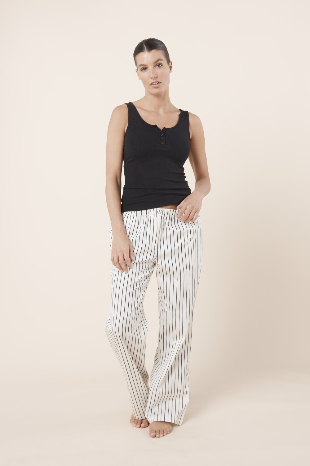 Woman wearing a black tank top and striped pants on a beige background