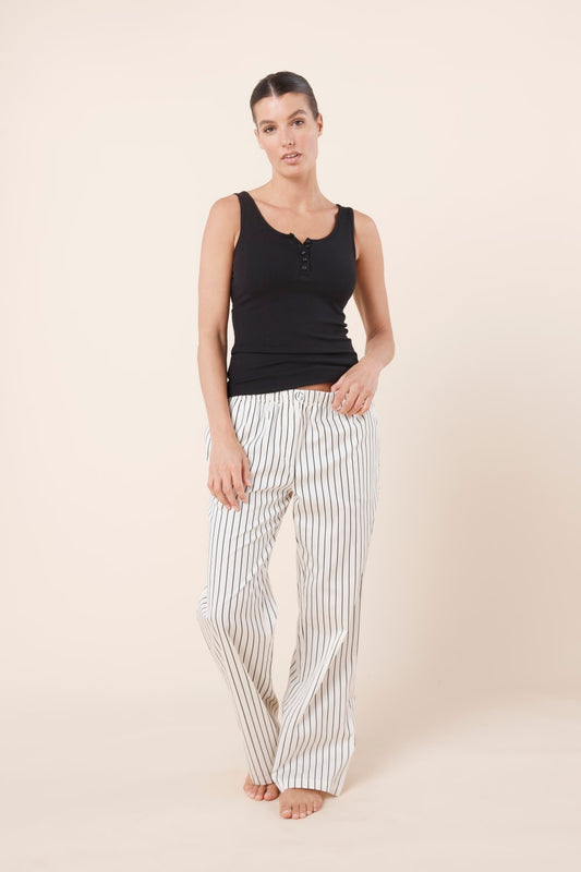 Woman wearing a black tank top and striped pants on a beige background