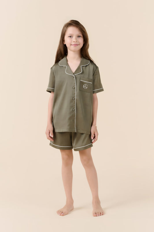 Girl wearing olive green Gingerlilly Sleepwear short pajama set with white trim, barefoot.