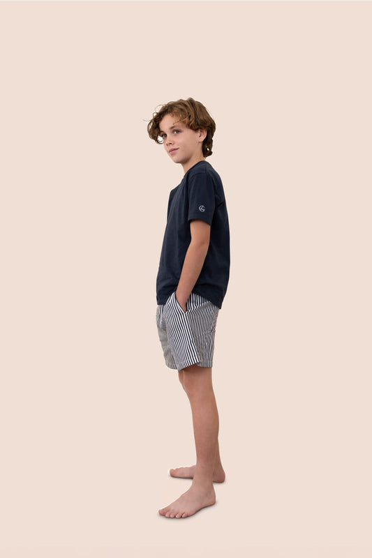 Young boy wearing a navy t-shirt and checkered shorts on a beige background