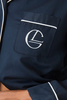 Close up of the embroidered logo on the chest pocket of the Susanna navy pyjama top, with white piping detail along the pocket edge.