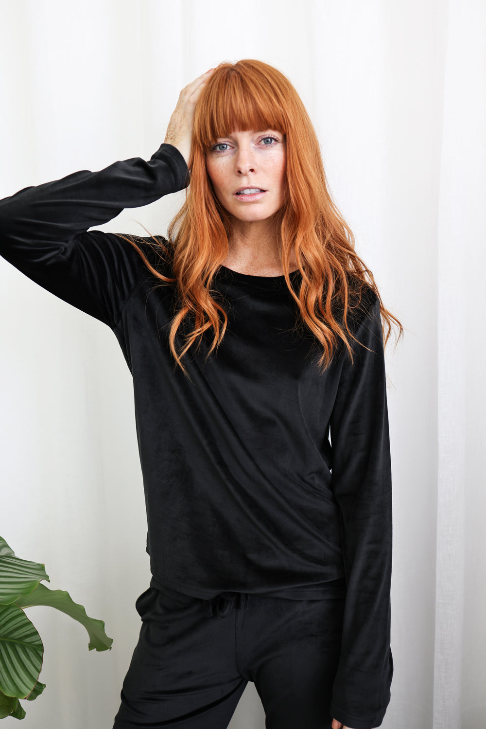 Woman in black Gingerlilly Sleepwear long sleeve loungewear set, standing by white curtain.