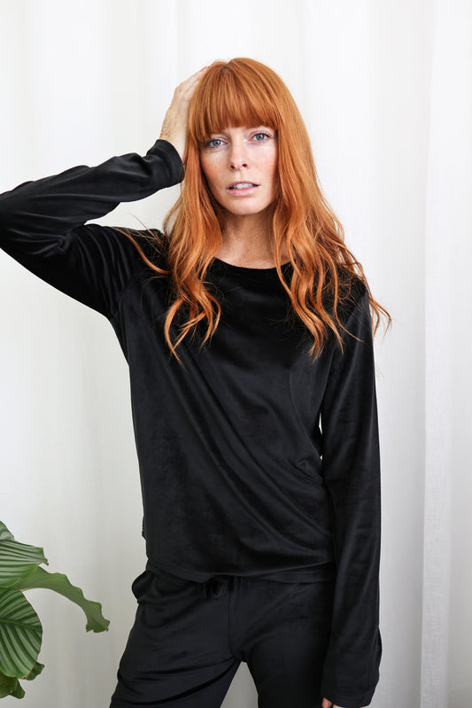 Woman in black Gingerlilly Sleepwear long sleeve loungewear set, standing by white curtain.