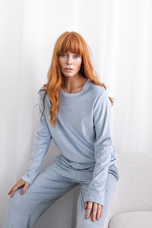 Woman in light blue Gingerlilly Sleepwear loungewear set, sitting on a chair, white background