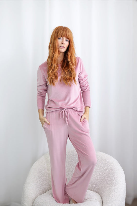 Woman in soft pink loungewear set from Gingerlilly Sleepwear, standing in a modern chair