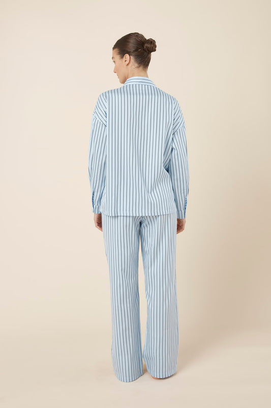 Woman wearing a blue striped willow cotton stripe pyjama PJ set on a beige background and back view