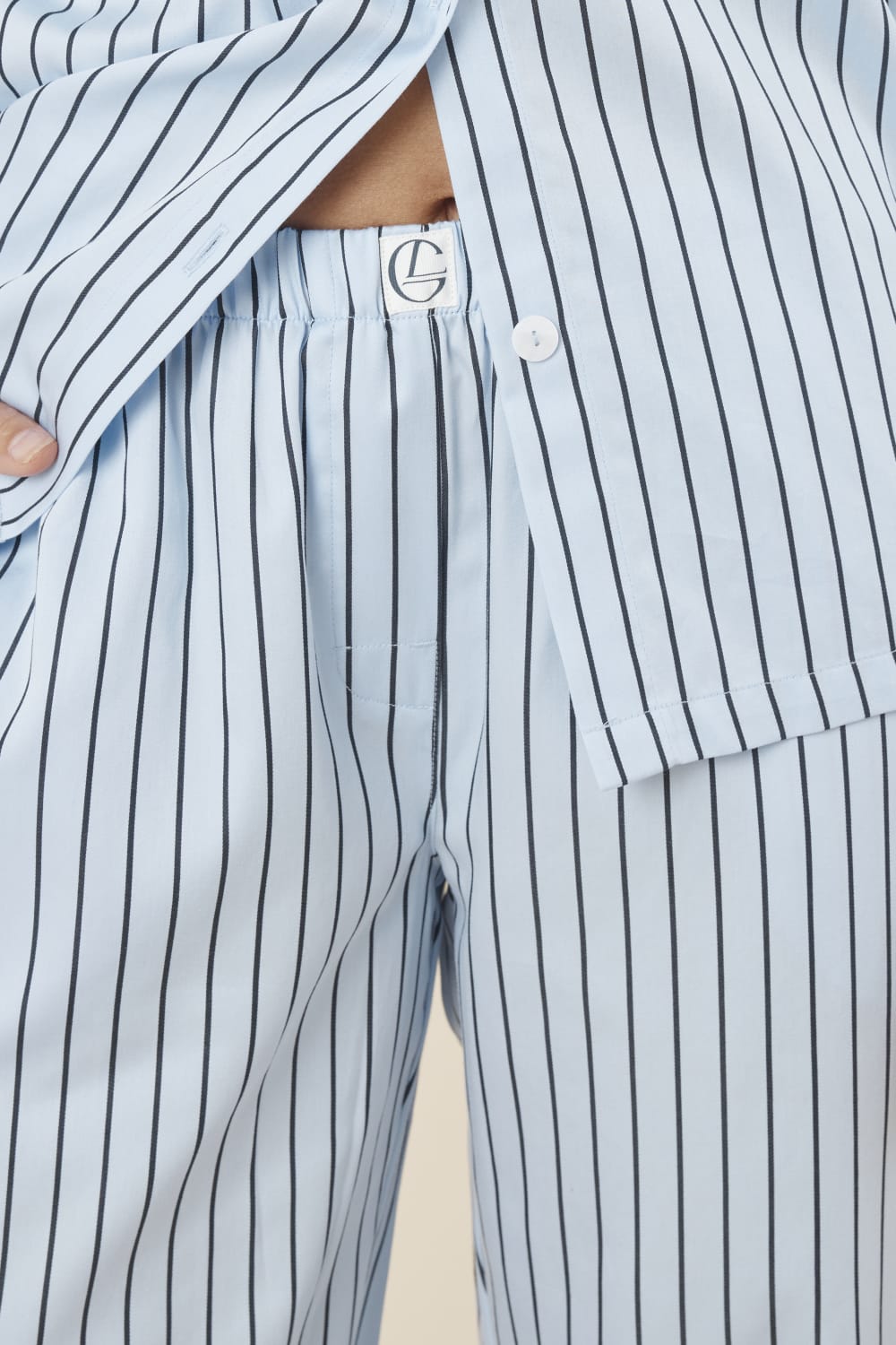 Woman wearing a blue striped willow cotton stripe pyjama PJ set with close up of waistline showing gingerlilly logo and white buttons