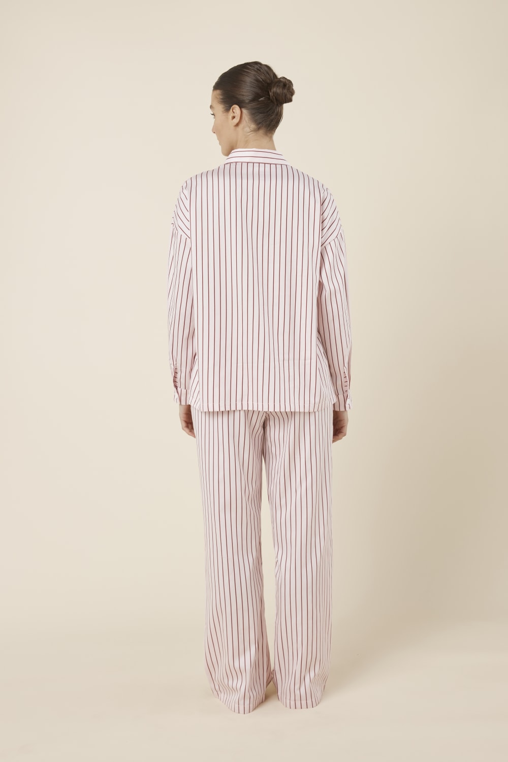 Woman wearing a pink striped willow cotton stripe pyjama PJ set in set on a beige background and back view