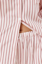 Close up waistline view of woman wearing a pink striped willow cotton stripe pyjama PJ set on a beige background showing the gingerlilly logo and white button