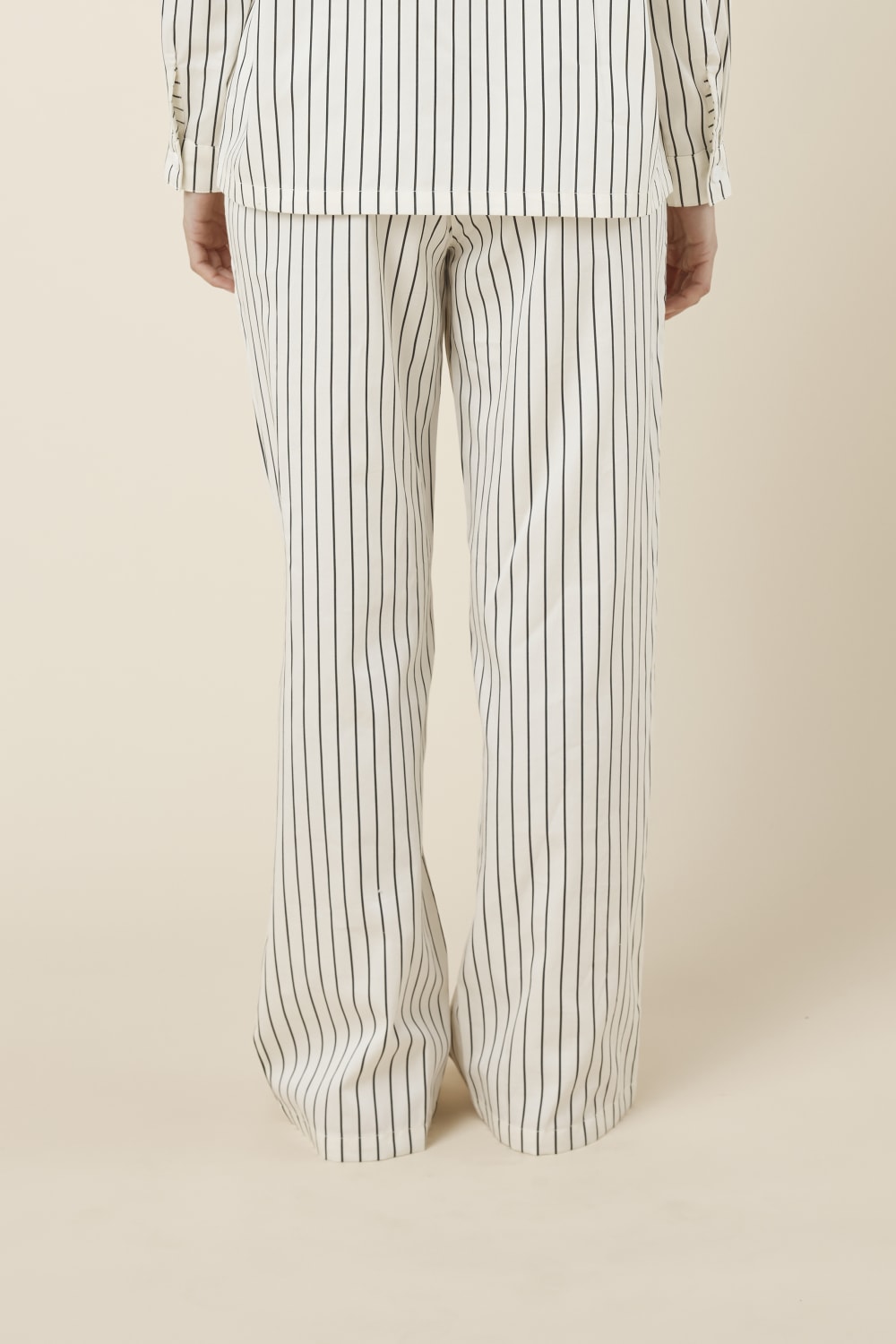 Woman wearing black and white striped willow cotton striped pyjama pants in ivory on a beige background back view