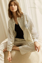 Woman wearing a white striped willow cotton striped pyjama set in ivory sitting on a couch