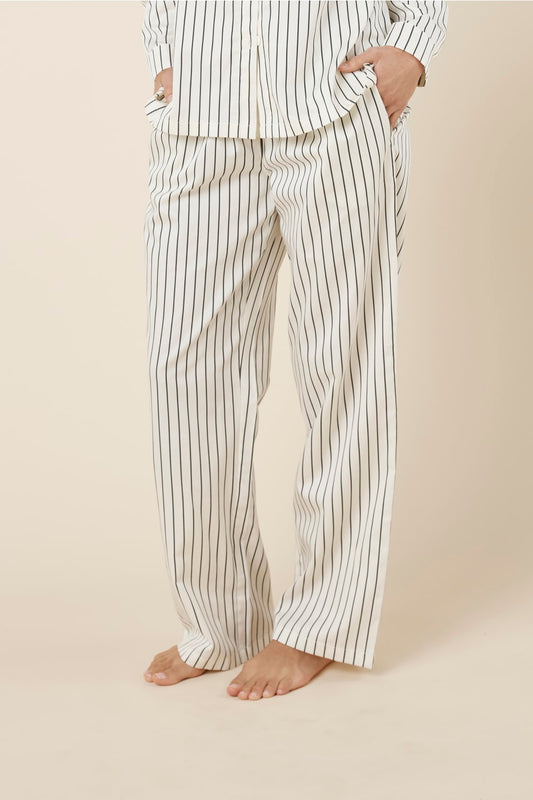 Woman wearing black and white striped willow cotton striped pyjama pj set in ivory on a beige background side view.