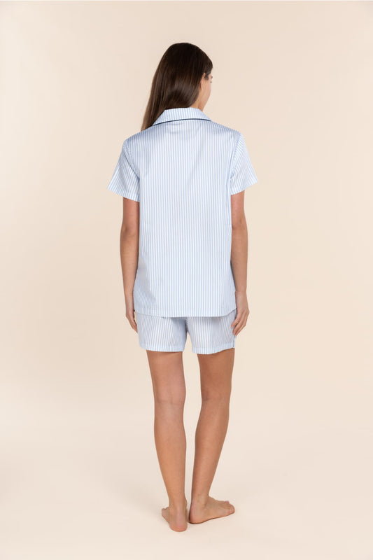 Woman wearing a light blue striped shirt and shorts set on a beige background
