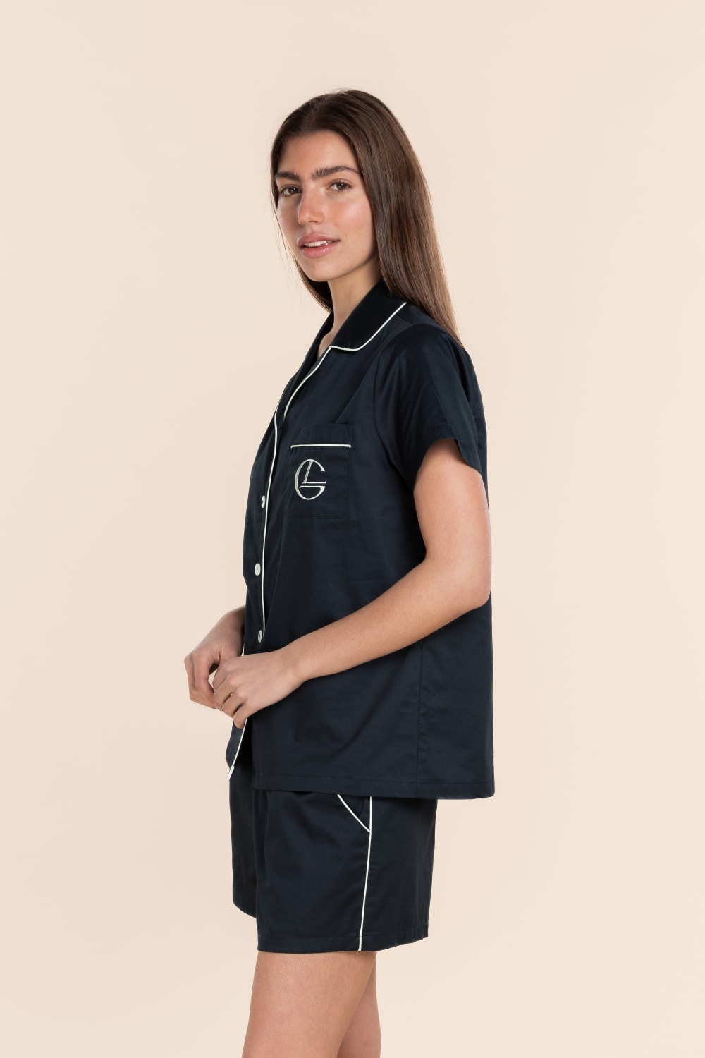 Woman wearing a navy outfit with white piping on a beige background
