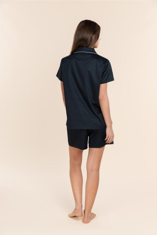 Person wearing a navy blue polo shirt and shorts set on a beige background