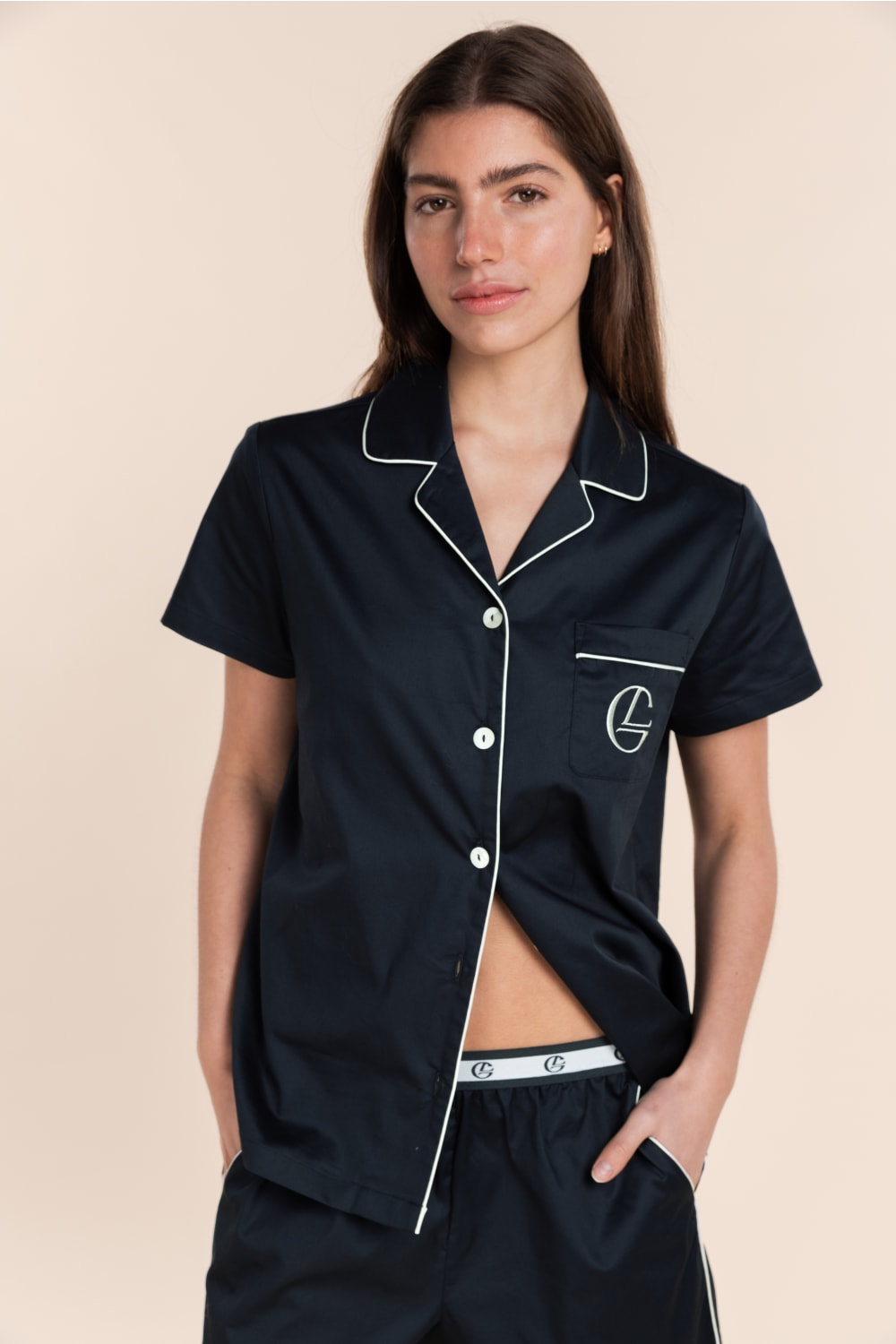 Woman wearing a navy pajama set with white trim on a beige background