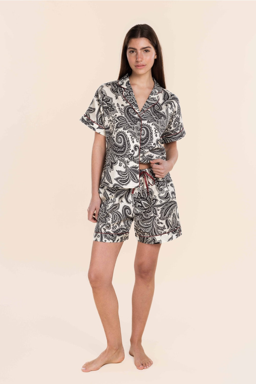 Woman wearing a black and white paisley pajama set on a beige background