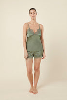 Woman front view wearing a green olive heather silky satin cami and short set with lace detail on a beige background