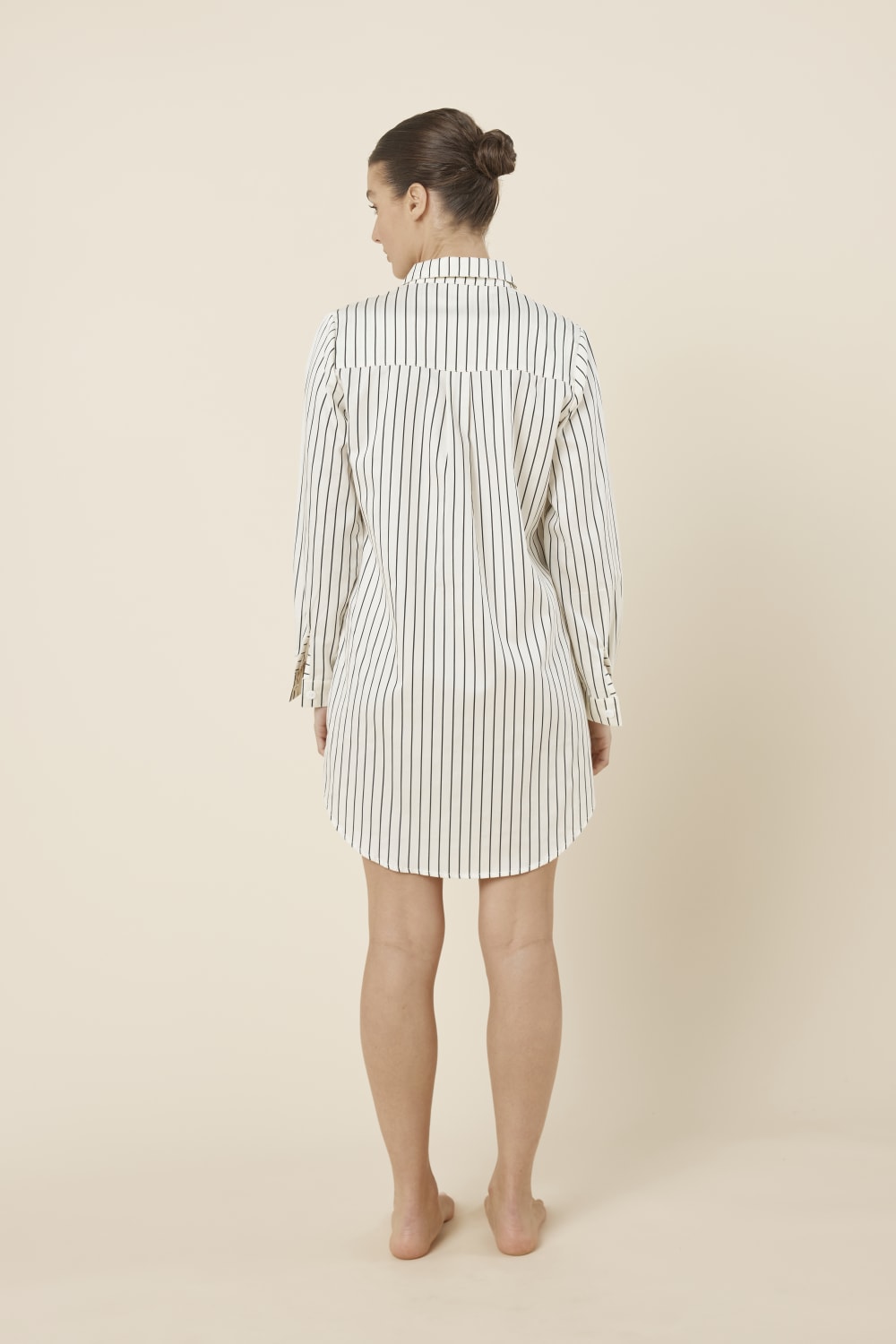 Woman wearing a lolita stripe night shirt in ecru black and ivory white stripe back view on a beige background