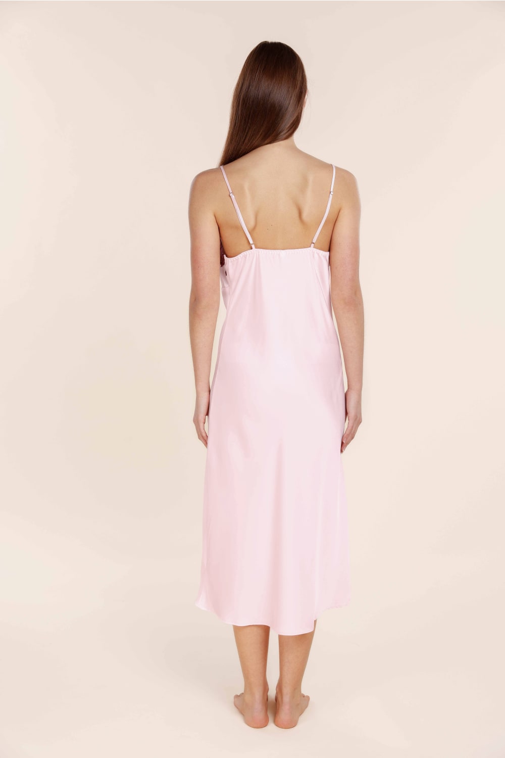 Woman wearing a light pink slip dress against a beige background