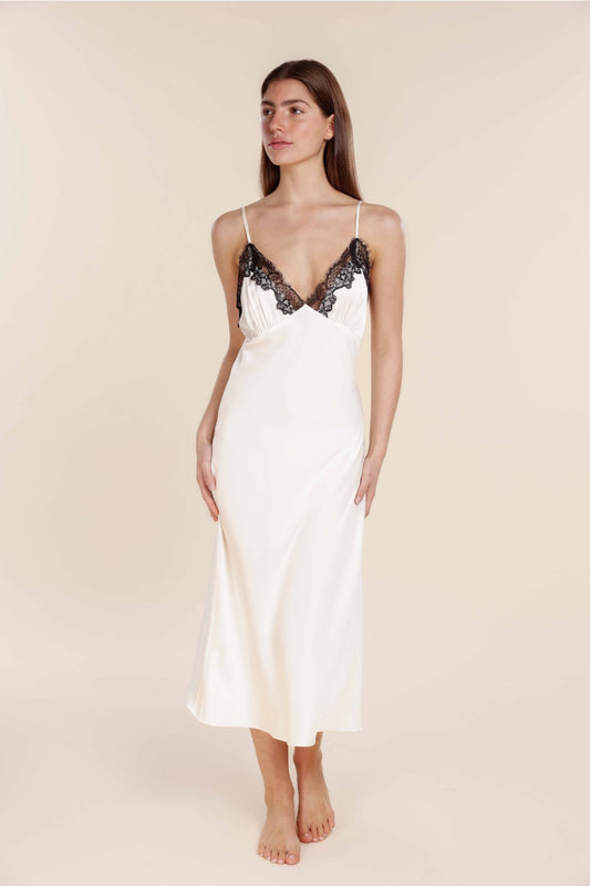 Woman wearing a white satin slip with black lace details on a plain background