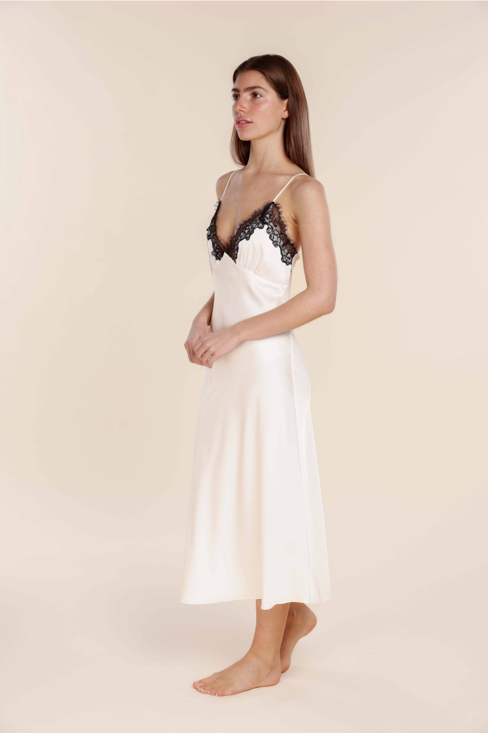 Woman wearing a white slip with black lace details on a plain background